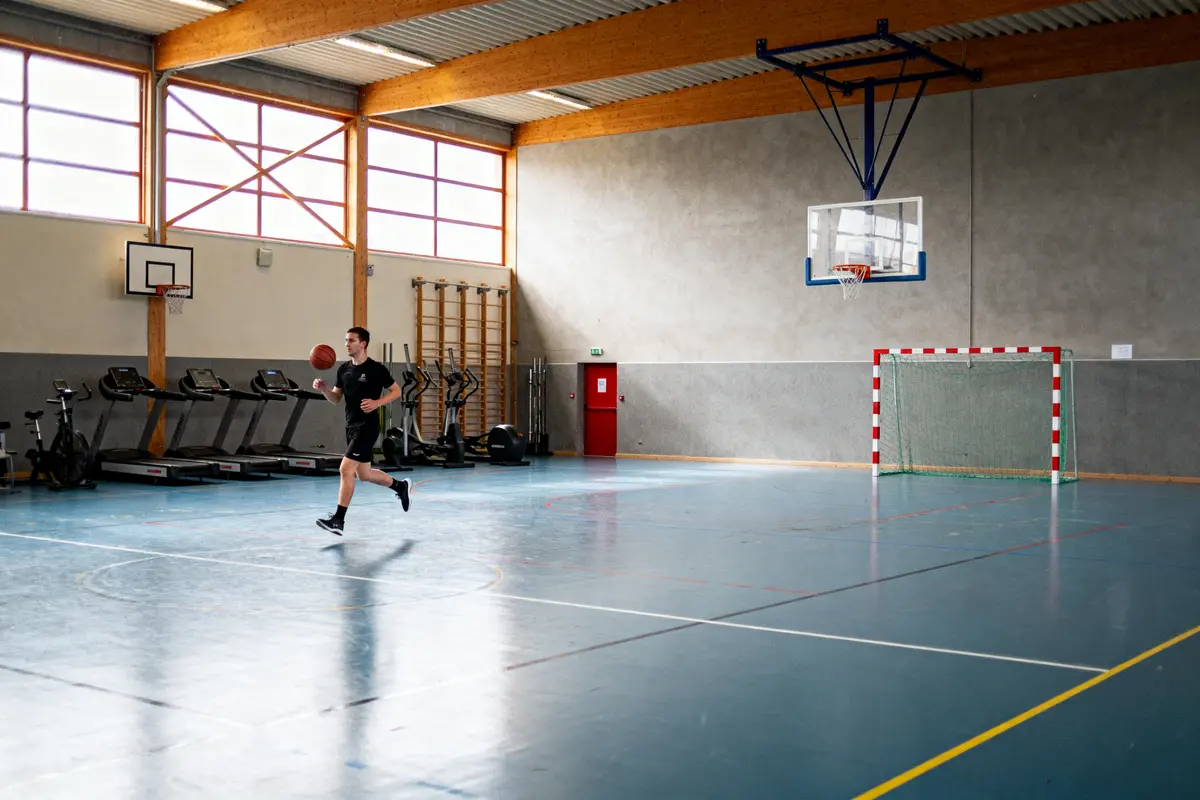 Un homme joue au basket dans un gymnase lumineux avec des équipements de fitness.