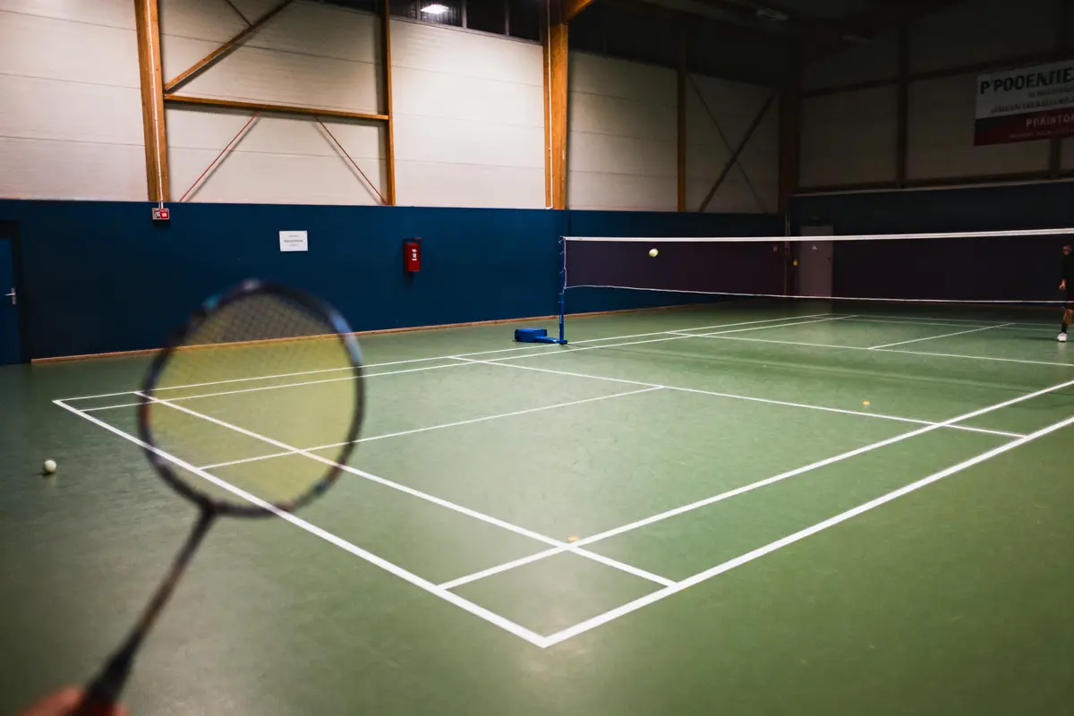 Raquette de badminton floue, terrain intérieur avec filet, mur bleu et luminosité artificielle.